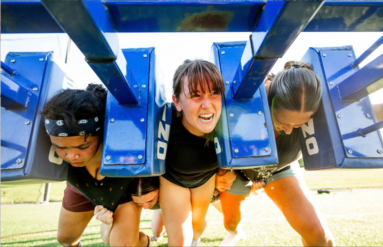 three womens rugby players grimace as they push a training sled